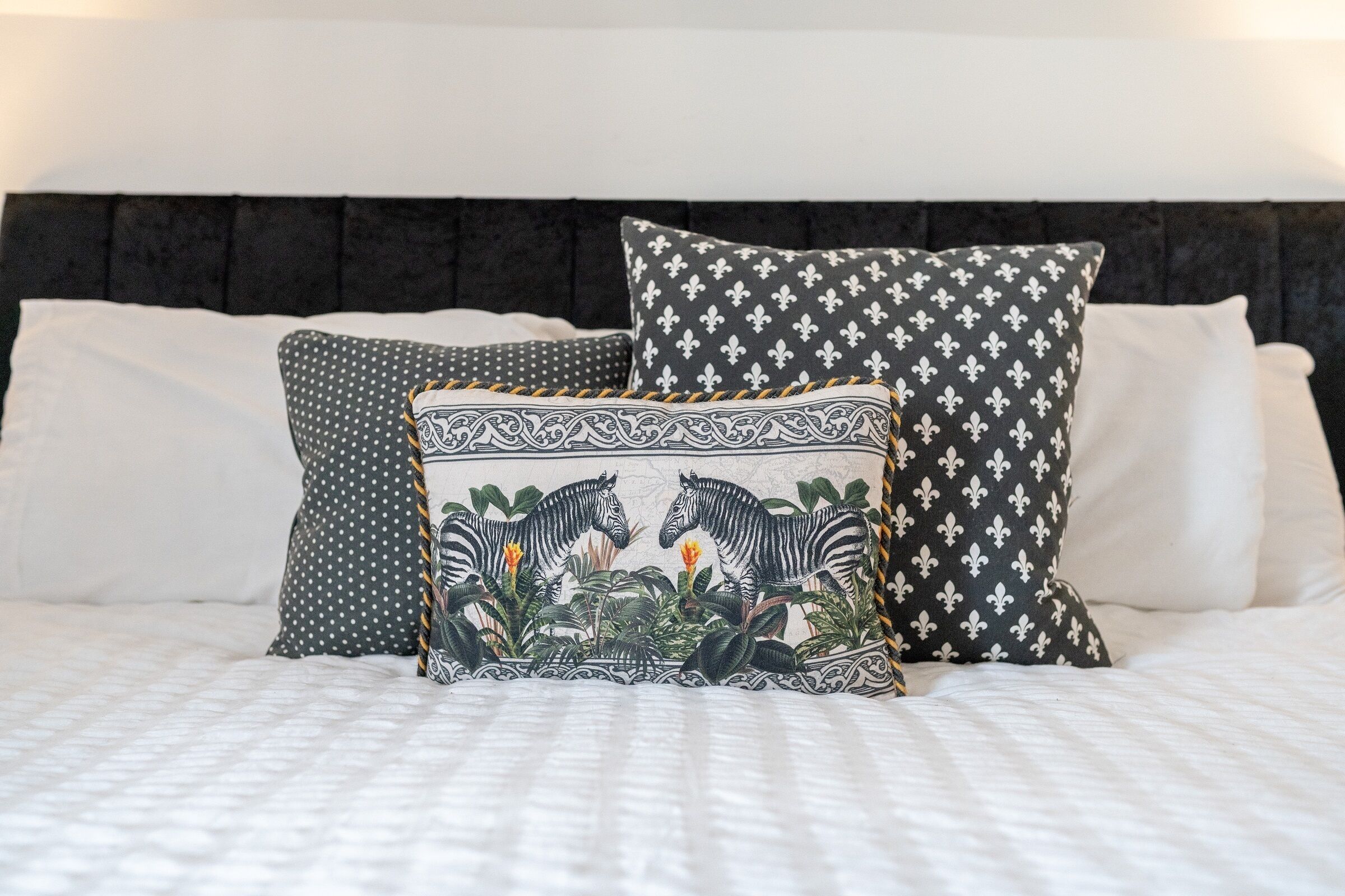 Una cama con ropa blanca y tres almohadas de diferentes diseños.