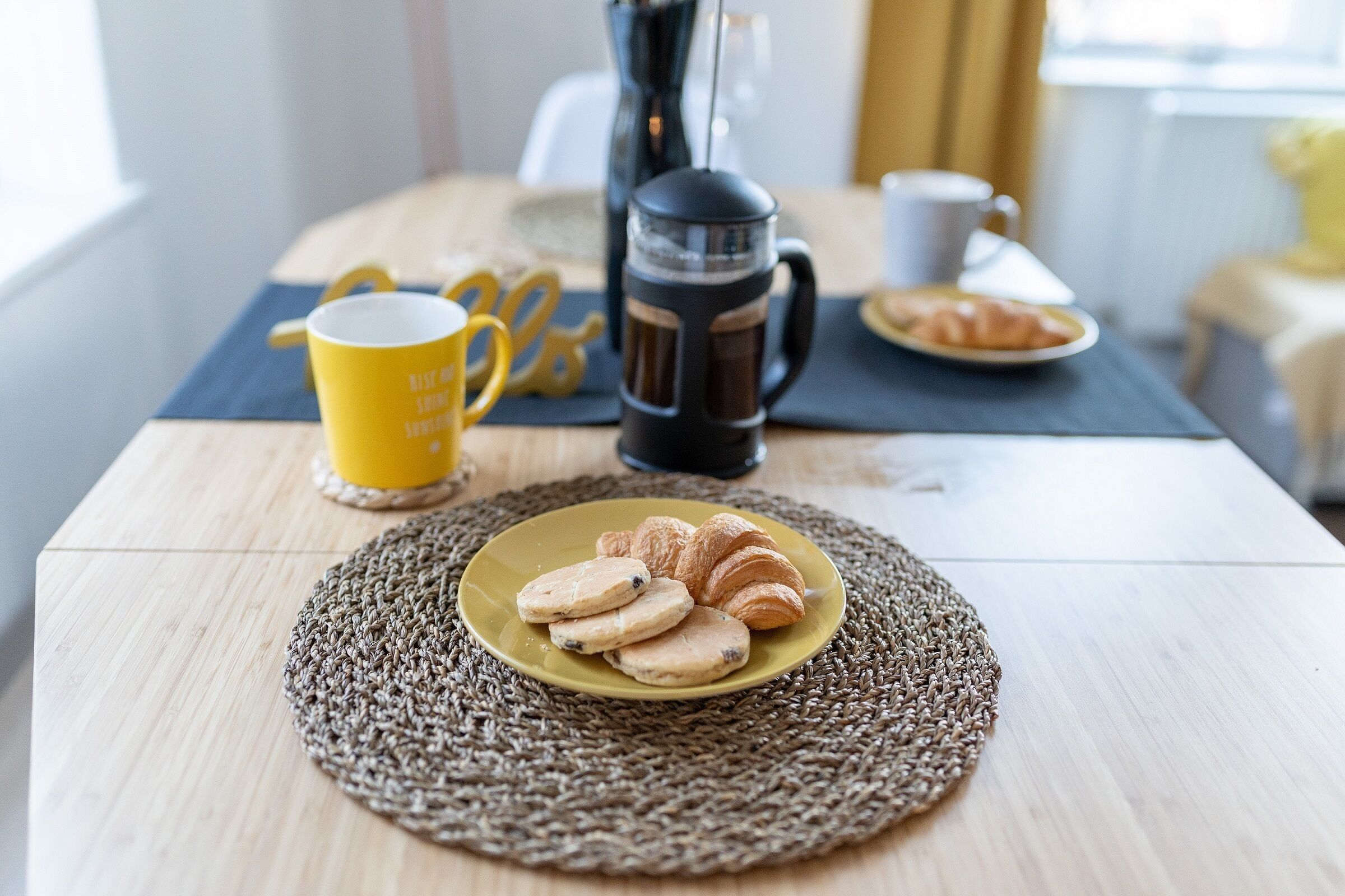 A breakfast setting with a plate of pastries and a coffee maker on a wooden table.