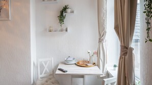 Un coin repas accueillant avec une table blanche, deux chaises, une télécommande et un plateau sur lequel se trouvent un vase et des verres.