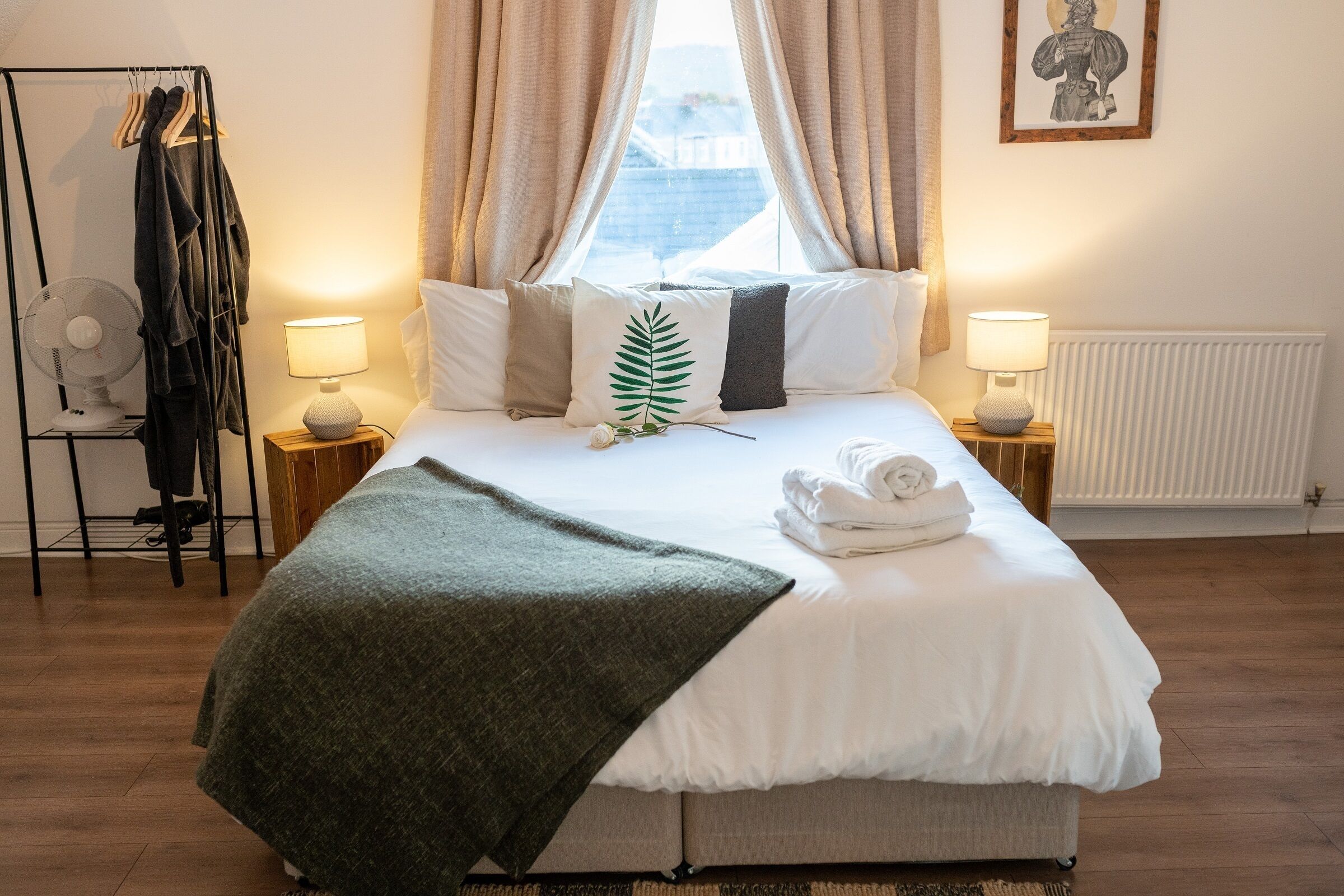 Un lit bien fait, avec du linge de lit blanc, un plaid vert et une vue sur l’extérieur par la fenêtre.