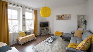 Un salon avec un canapé, une table basse, un téléviseur et une suspension jaune.