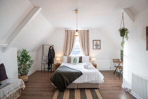 A bedroom with a bed, bedside lamps, a radiator, a hanging plant, a coat rack, and a window with curtains. - Phénix Central - Huge 3 Bed Apt. (Cardiff)