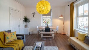 Un salon comprenant une table à manger, deux canapés, un luminaire suspendu jaune et une fenêtre avec des rideaux.