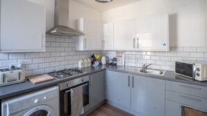 Une cuisine moderne avec des meubles blancs, une cuisinière à gaz, un four à micro-ondes et un lave-linge.