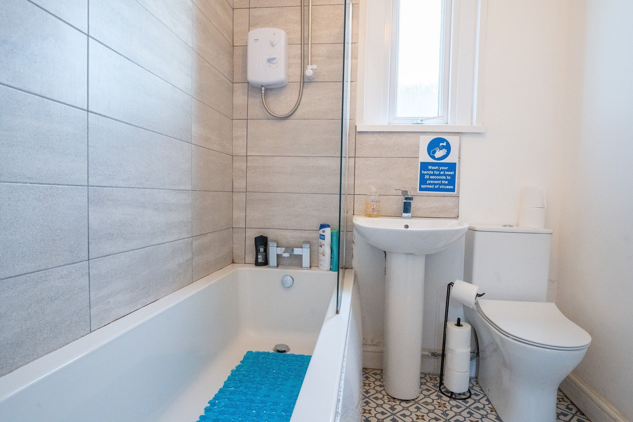 A bathroom with a bathtub, a sink, and a toilet. There is a sign above the sink indicating handwashing instructions.