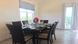 A dining area with a rectangular table set for six, surrounded by wicker chairs with cushioned seats. - Tranquil Villa near Long Bay Beach, Pool & Sunsets (Long Bay Hills)