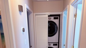 Une buanderie équipée de deux machines à laver et deux sèche-linge superposés, avec un plancher en bois et des murs blancs.