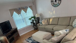 Un salon comprenant un canapé, un téléviseur, une table basse, un tapis à motifs et une horloge murale.