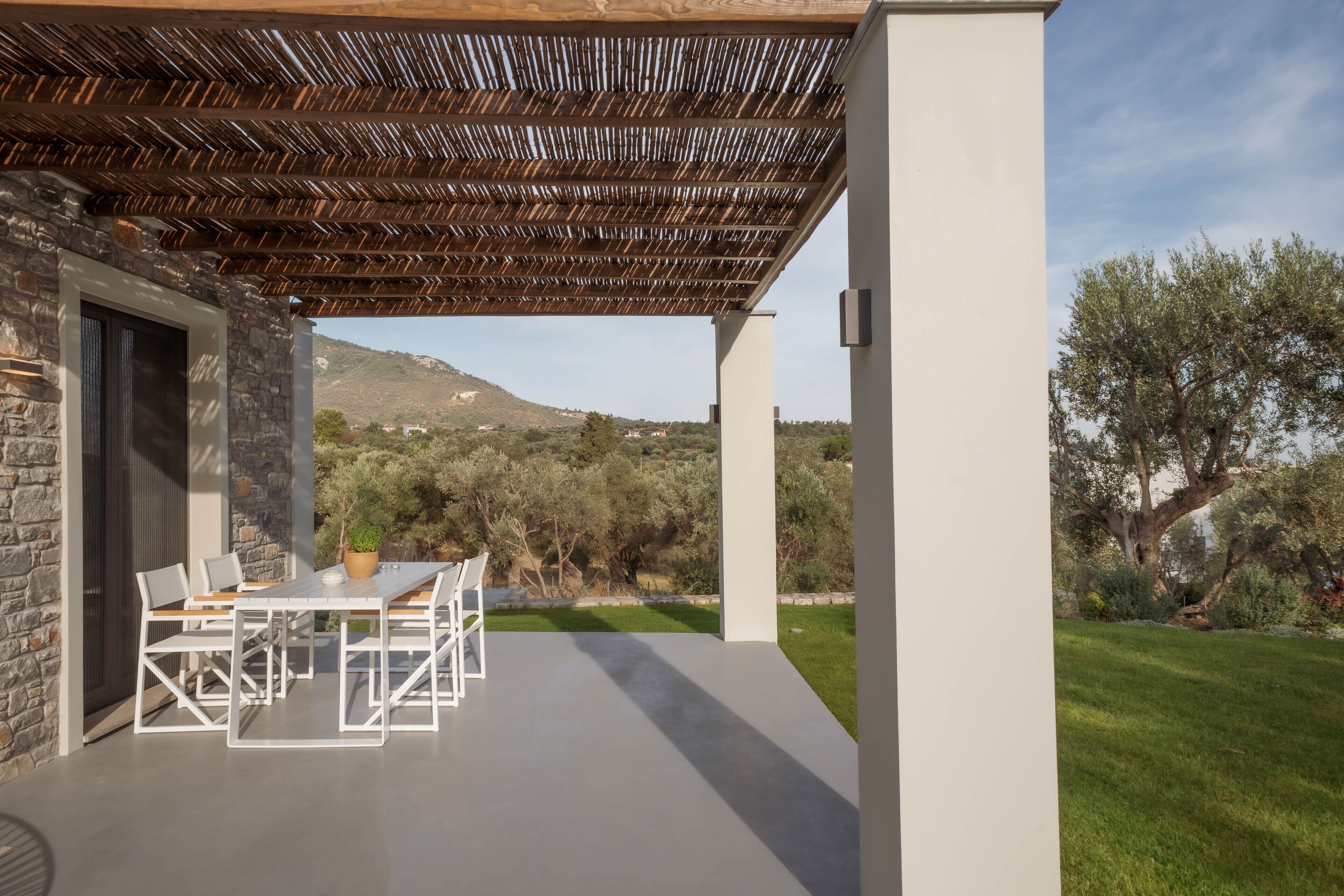 Une terrasse couverte avec un mur en pierre, une table avec des chaises et une vue sur un paysage verdoyant, avec des arbres et des collines.