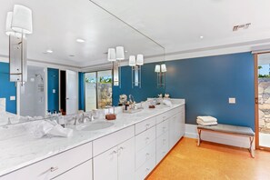 A modern bathroom with a long vanity, a large mirror, and a bench.