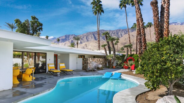 A modern pool area with a clear view of mountains, a stone wall, and yellow chairs.