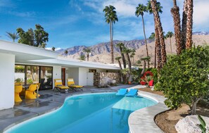 A modern pool area with a clear view of mountains, a stone wall, and yellow chairs. - Timeless Retreat - Mountain and Golf Course Views! (Palm Springs)