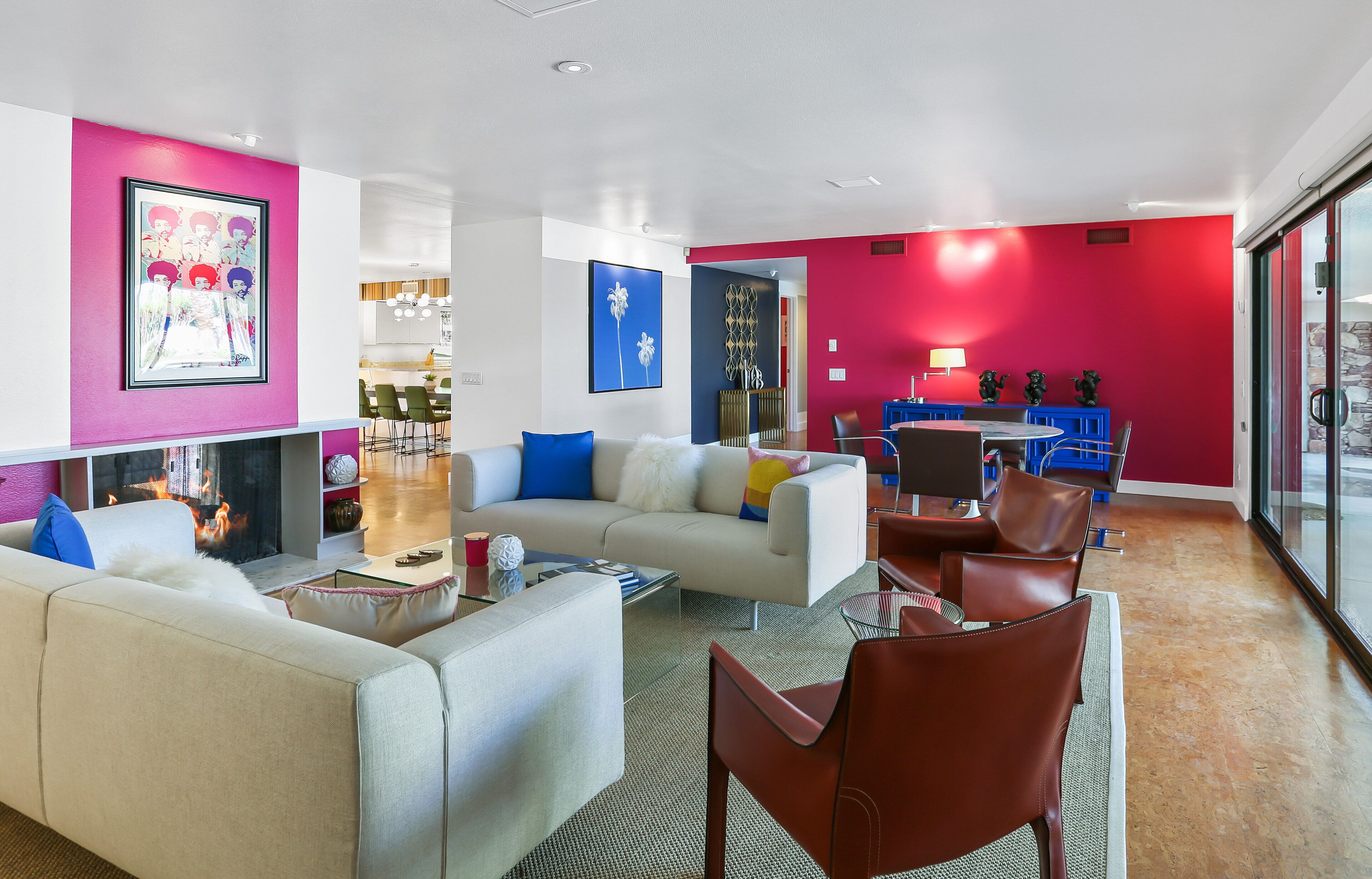A modern living room with a fireplace, a sofa, a dining area with blue chairs, and a red accent wall.