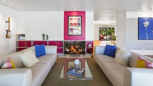 A modern living room with two sofas, a fireplace, a guitar, and a bookshelf.