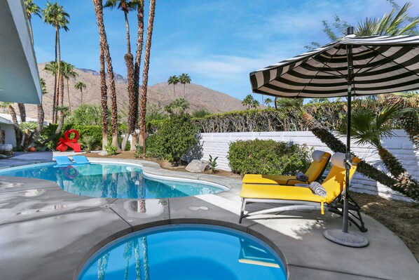 A swimming pool with a curved design, surrounded by palm trees and a mountain in the background.