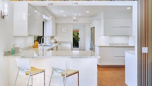 A modern kitchen with a central island, bar stools, white cabinetry, and a striped wall design.