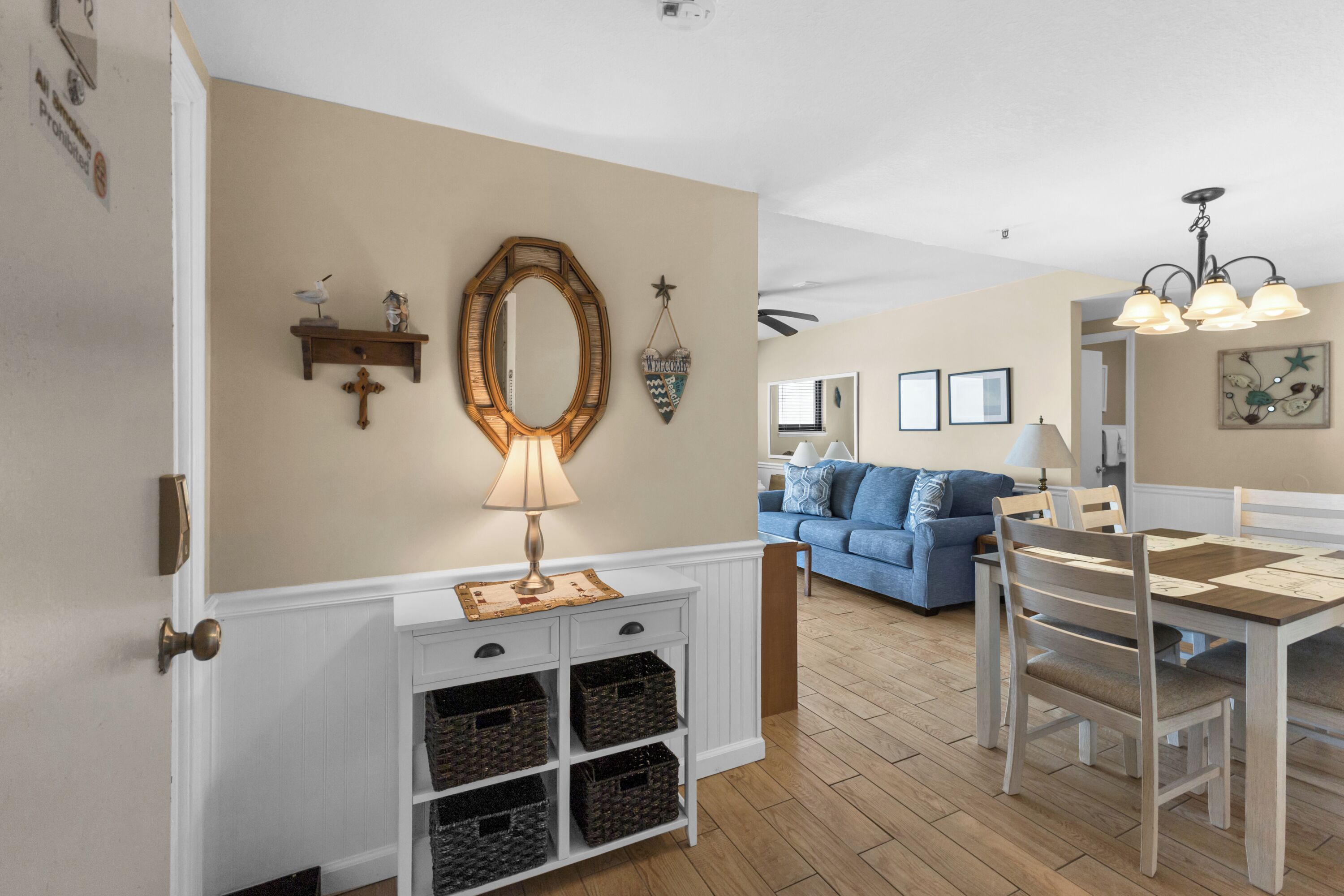 A dining area with a wooden table and chairs, a white console table with baskets, and a wall-mounted mirror.