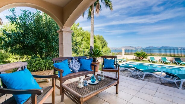 Eine Terrasse im Freien mit Pool, Holzmöbeln und Blick aufs Meer.