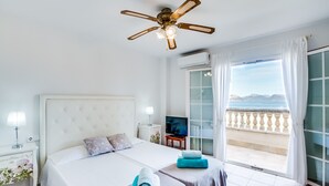 Ein Hotelzimmer mit Bett, Deckenventilator, Fernseher, Balkon mit Meerblick und einem Fenster mit Vorhängen.