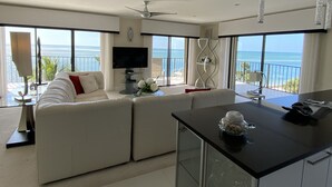 Ein modernes Wohnzimmer mit einer Couch, einem Fernseher und einem Balkon mit Meerblick.