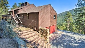 A rustic wooden cabin with a red door, a staircase leading to a deck, and a view of a forested hillside. - The Evergreen Gem| Mountain Experience Retreat (Evergreen)