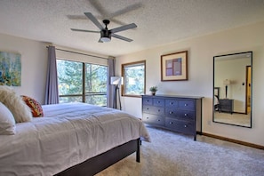 Quarto com cama, cômoda e grandes janelas.