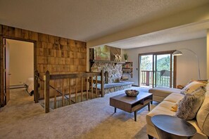 A spacious living area with a stone fireplace, a wooden staircase, and a large window offering a view of the outdoors. - The Evergreen Gem| Mountain Experience Retreat (Evergreen)