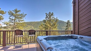 A hot tub on a wooden deck with two chairs, overlooking a forested area. - The Evergreen Gem| Mountain Experience Retreat (Evergreen)