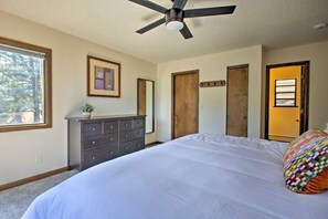 A bedroom with a bed, dresser, ceiling fan, and a door leading to another room.
