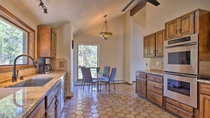 A kitchen with hexagonal tile flooring, wooden cabinets, stainless steel appliances, and a dining area with chairs. - The Evergreen Gem| Mountain Experience Retreat (Evergreen)