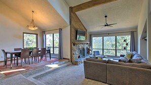 A spacious living area with a stone fireplace, a large window, and a ceiling fan. - The Evergreen Gem| Mountain Experience Retreat (Evergreen)