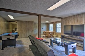 A room with a pool table, a sofa, a coffee table, a TV, and a dining area with chairs.