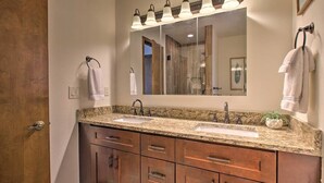 A bathroom with a double sink vanity, wooden cabinets, and a large mirror with lights above. - The Evergreen Gem| Mountain Experience Retreat (Evergreen)