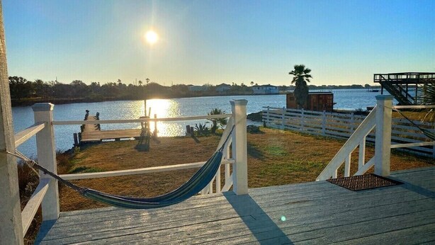 A wooden deck with a hammock, a view of the water, and a distant building. - Sunny San Leon Casita!! (San Leon)
