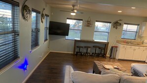 A spacious living area with a large couch, a kitchen with white cabinets, and a dining area with stools. - Sunny San Leon Casita!! (San Leon)
