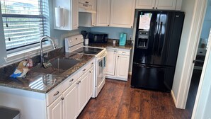 A kitchen with white cabinets, a black refrigerator, a stainless steel sink, and a window with blinds. - Sunny San Leon Casita!! (San Leon)