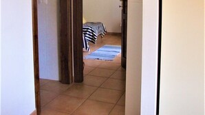 Een smalle gang met een bed aan het einde, een spiegel aan de muur en een koelkast aan de rechterkant.