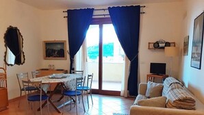 Een woonkamer met een bank, een eettafel met stoelen, een televisie en een balkon met gordijnen.
