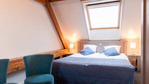 A bedroom with a sloped ceiling, a bed with blue bedding, two bedside lamps, and a window.