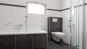 A modern bathroom with a bathtub, toilet, and glass shower enclosure.