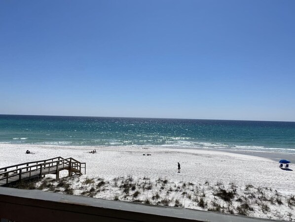 A beach with a wooden walkway leading to the water, a person walking, and a beach umbrella. - Right ON world’s whitest beach, Pensacola Beach, Florida. (Pensacola Beach)