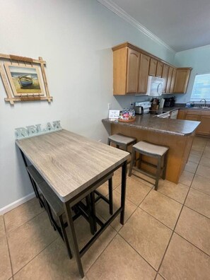 A kitchen with a wooden table, two stools, and a built-in island with a sink. - Right ON world’s whitest beach, Pensacola Beach, Florida. (Pensacola Beach)