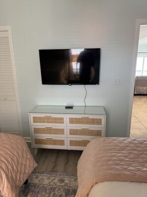 A bedroom with a TV mounted on the wall, a white dresser, two beds with pink bedding, and a patterned rug. - Right ON world’s whitest beach, Pensacola Beach, Florida. (Pensacola Beach)