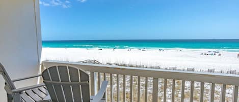 A balcony with a view of a beach, a chair, and a railing.