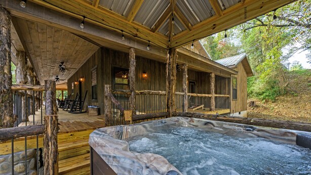 Eine rustikale Holzhütte mit Whirlpool, einer Holzterrasse und einer überdachten Veranda.