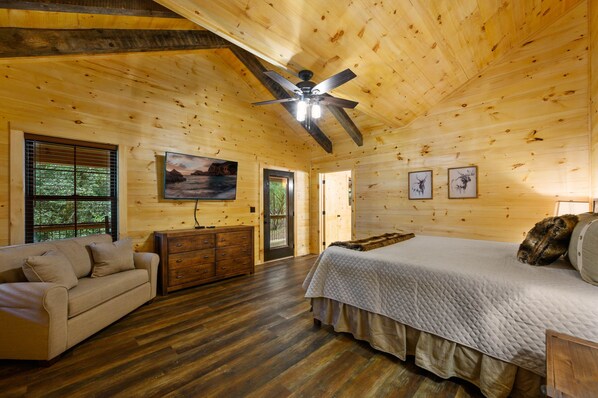 A wooden cabin bedroom with a bed, a sofa, a dresser, and a ceiling fan. - Private Creekside Cabin ~SEASONAL POOL, GAMES, FIRE PIT on 1.4 acres🕹️🔥 (Pigeon Forge)