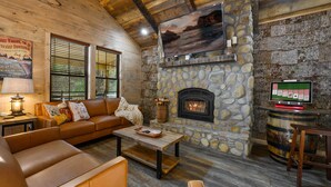 L’intérieur d’un chalet chaleureux, avec une cheminée en pierre, des meubles en cuir et un téléviseur.