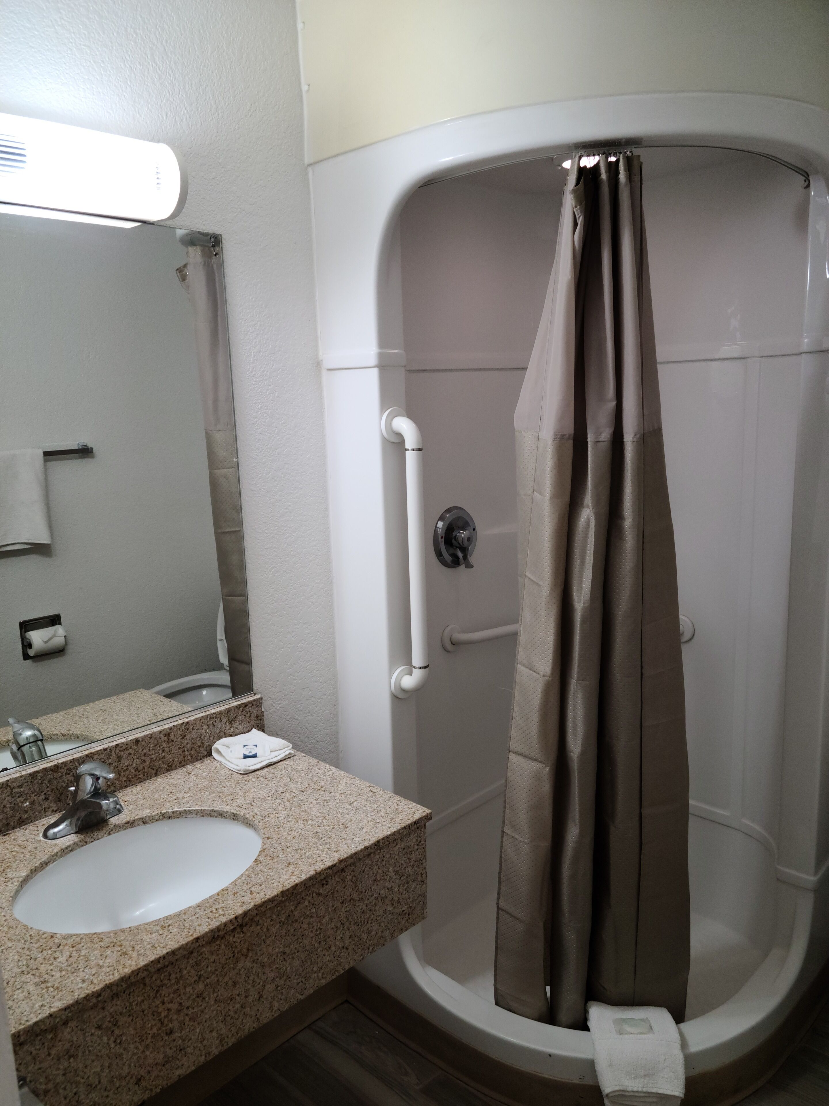 A bathroom with a sink, mirror, shower curtain, and grab bars.