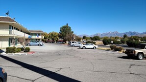 A parking lot with several cars, a building with a blue sign, and mountains in the background. - Motel 9 Las Cruces (Las Cruces)