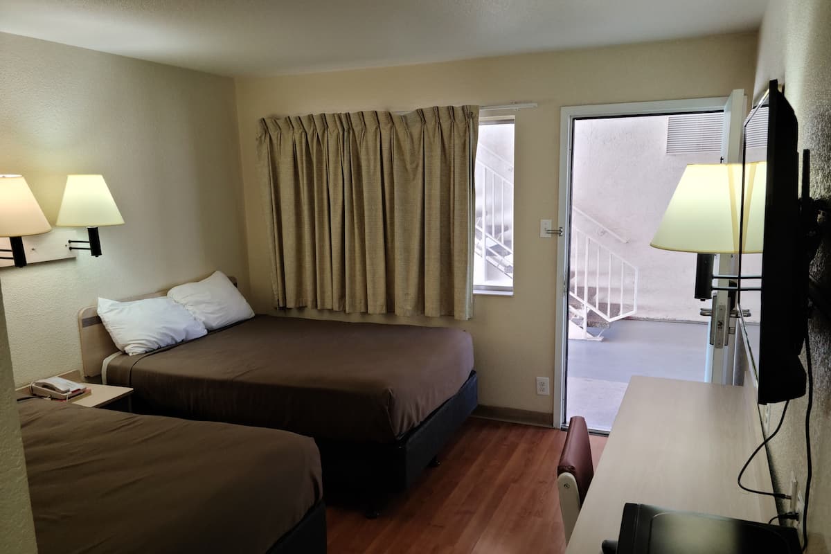 A hotel room with two beds, a desk, a chair, and a window with curtains.